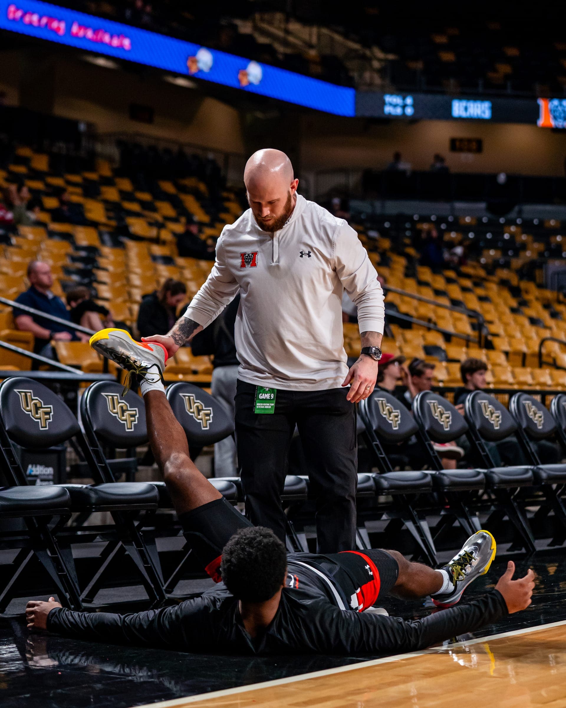 Colin DeClark assisting a basketball player with a courtside hamstring stretch