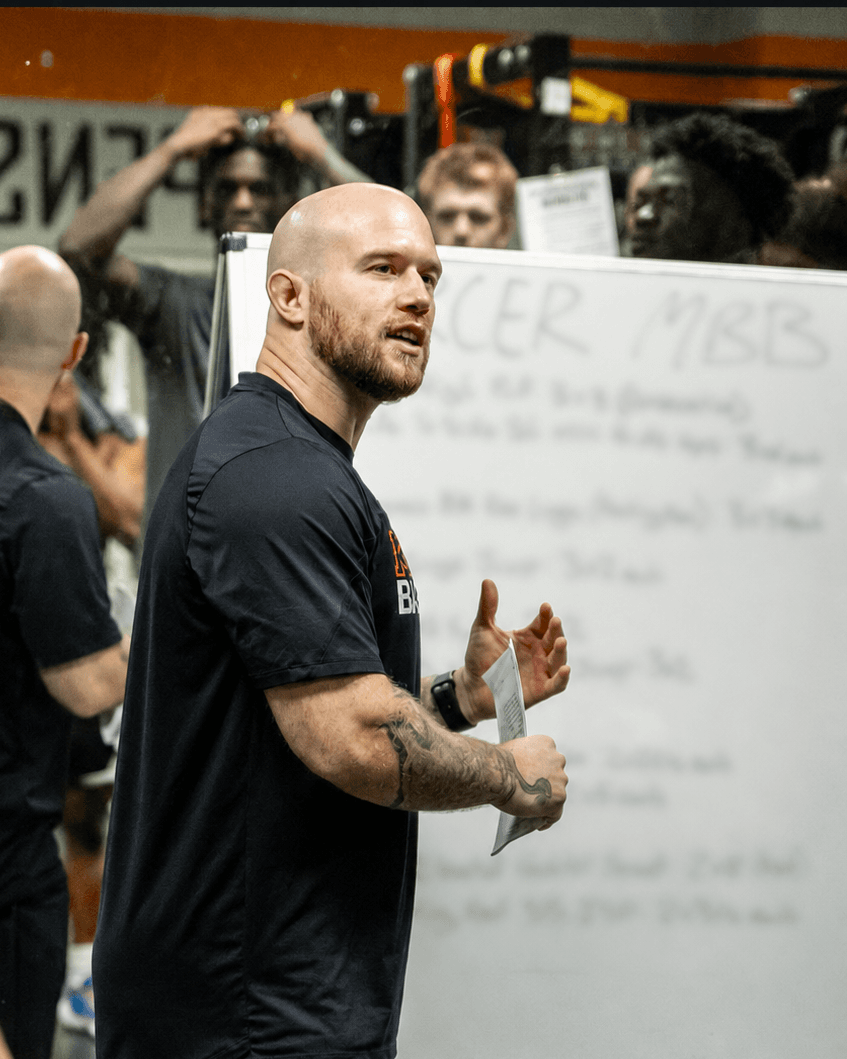 Colin DeClark coaching a workout session, standing in front of a whiteboard with a practice plan